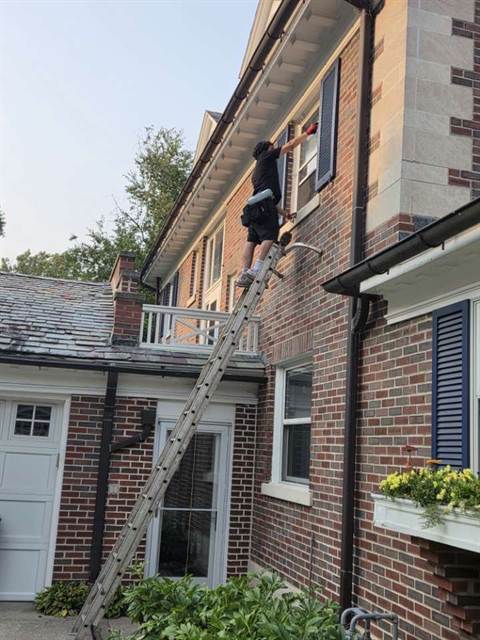 Ladder set against a brick house, cleaning a second-storey window above the garage.