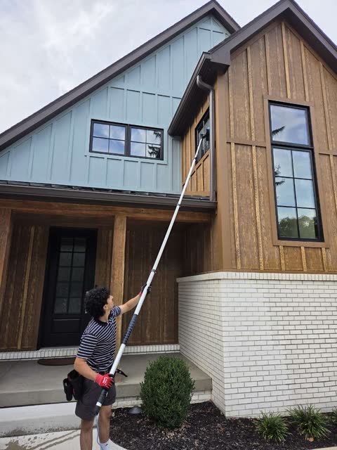 One of us on a front step, reaching a gable window with a water-fed pole.
